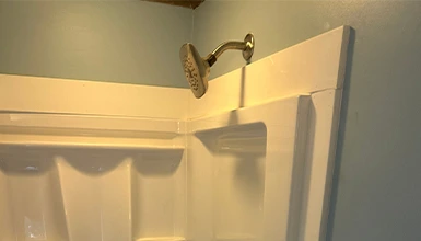 Close-up of a white fiberglass shower stall with a bronze shower head.