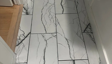 Modern bathroom tiling installation featuring white marble-effect tiles with dark veining.