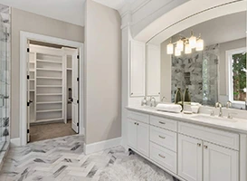 Bright bathroom with white cabinets, marble floor, and walk-in closet.