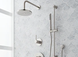 Modern brushed nickel shower system with rain shower head and handheld sprayer on marble tile.