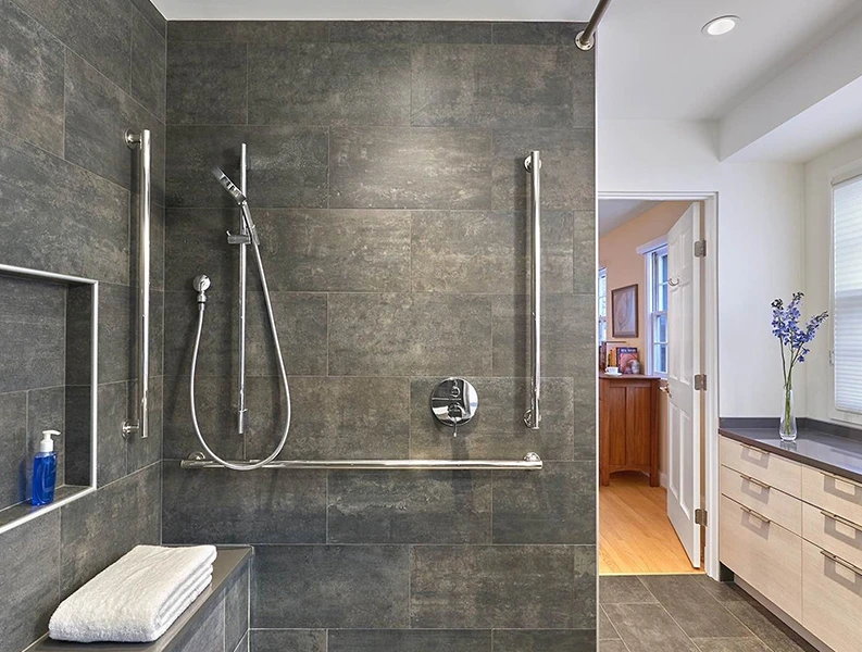 Modern bathroom shower remodel with gray tile, grab bars, and a built-in shower seat.