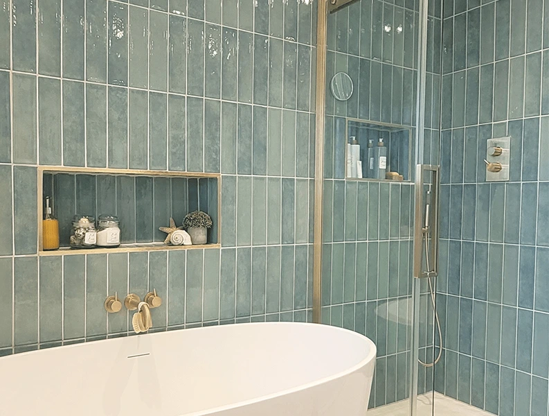 Modern bathroom with blue vertical tiles, freestanding tub, and glass shower enclosure.