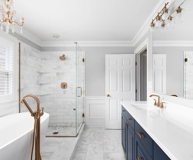 Bright bathroom with marble shower, freestanding tub, navy vanity, and brass fixtures.