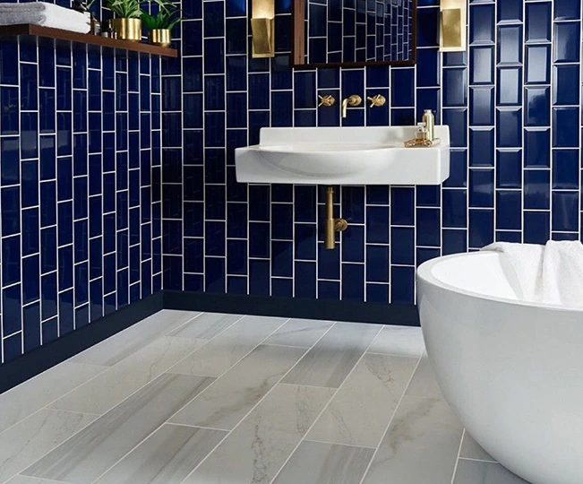 deep blue subway tiles, white sink and tub, light wood-look floor.