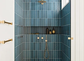 Blue custom shower tiling with a built-in shelf and gold fixtures.